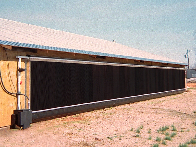 Long agricultural building with a sloped roof and large black installation resembling solar panels along its side.