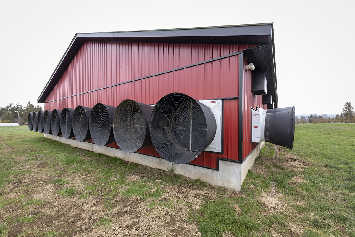 Side of a large red building with multiple industrial fans mounted along the wall, likely for ventilation.