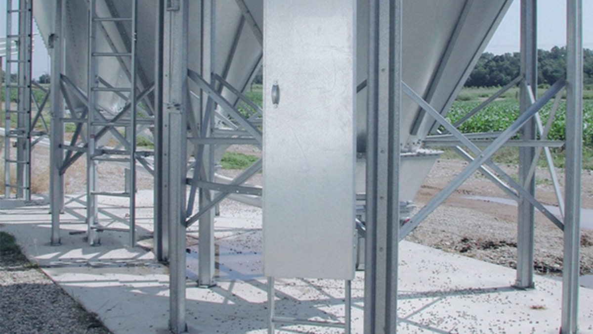 Green outline icon of industrial silos, representing storage or agricultural processing facilities.